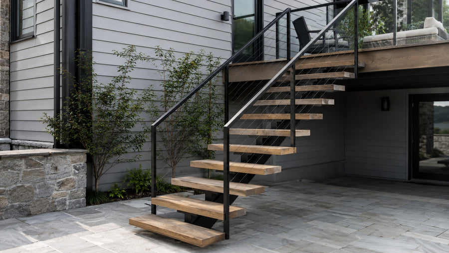 Exterior floating stairs with wood treads and cable railing connecting a modern home deck to a stone patio