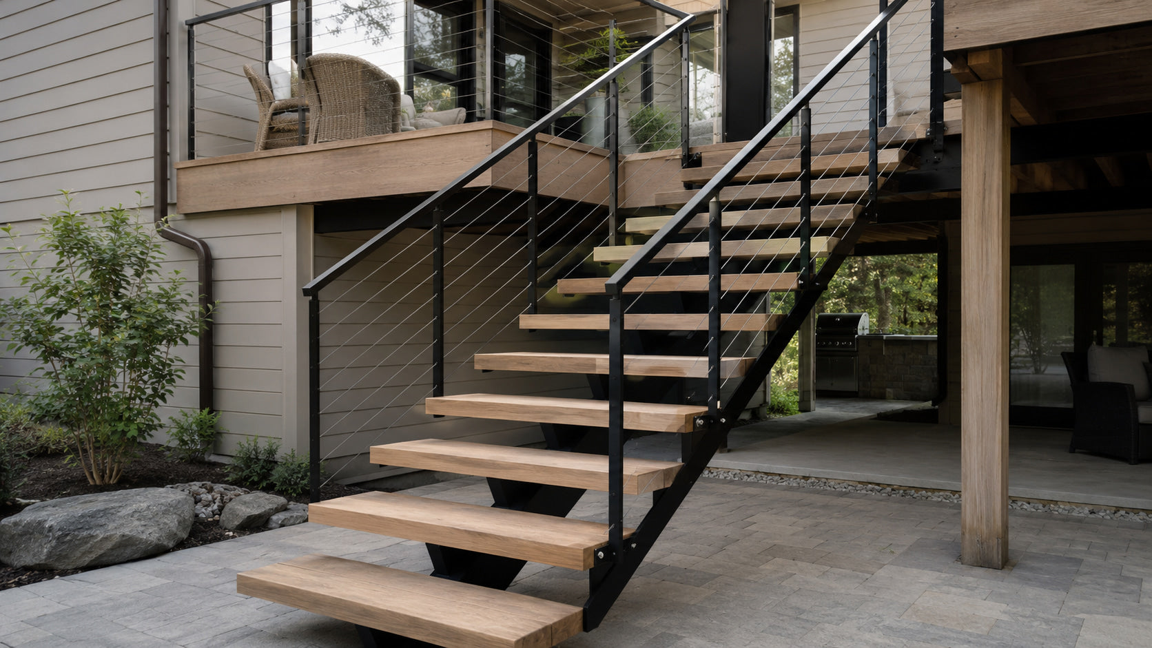 Custom floating deck stairs with wood treads and dark steel supports connecting a modern raised deck to a landscaped patio