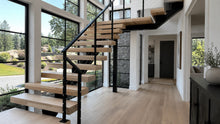 Modern floating stairs with cable railing, white oak treads, and a matte black steel mono stringer in a bright residential interior.