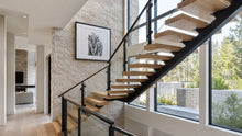Floating stairs with glass railing, warm white oak treads, and a matte black steel mono stringer in a bright modern home interior.