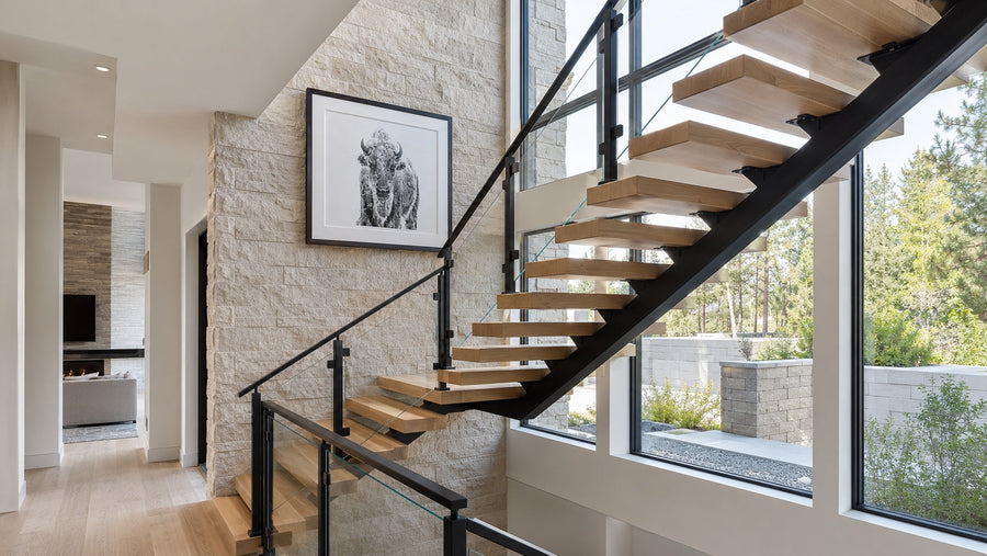 Floating stairs with glass railing, warm white oak treads, and a matte black steel mono stringer in a bright modern home interior.