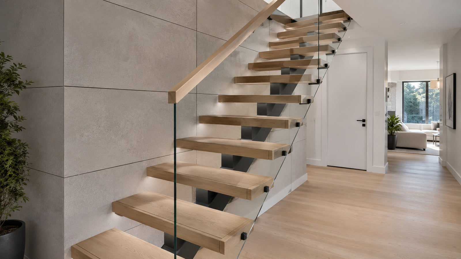 Modern floating stairs with warm white oak wood treads, matte black steel support, and clear glass railing in a refined residential interior.